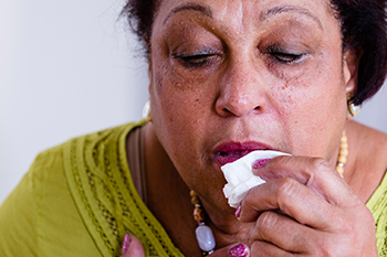 Unter einem Schub leidende Frau, die ein Taschentuch zum Gesicht f&uuml;hrt