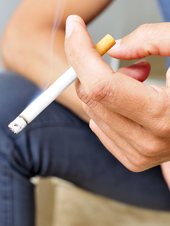 Hand, die eine angez&uuml;ndete Zigarette h&auml;lt